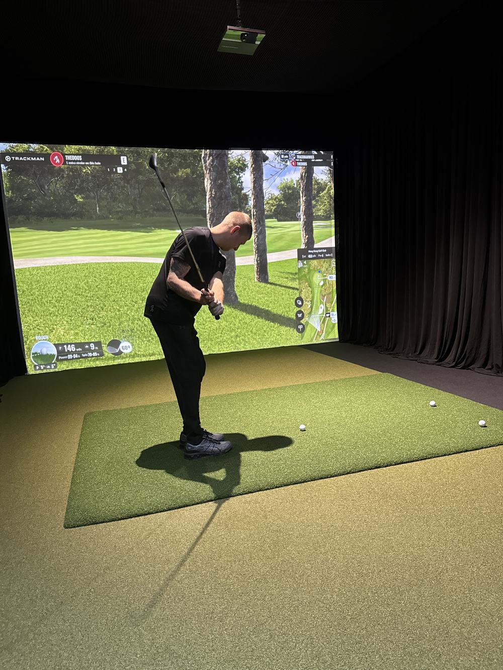 Golfer mid-swing on a wooded fairway simulation at TOUR XP